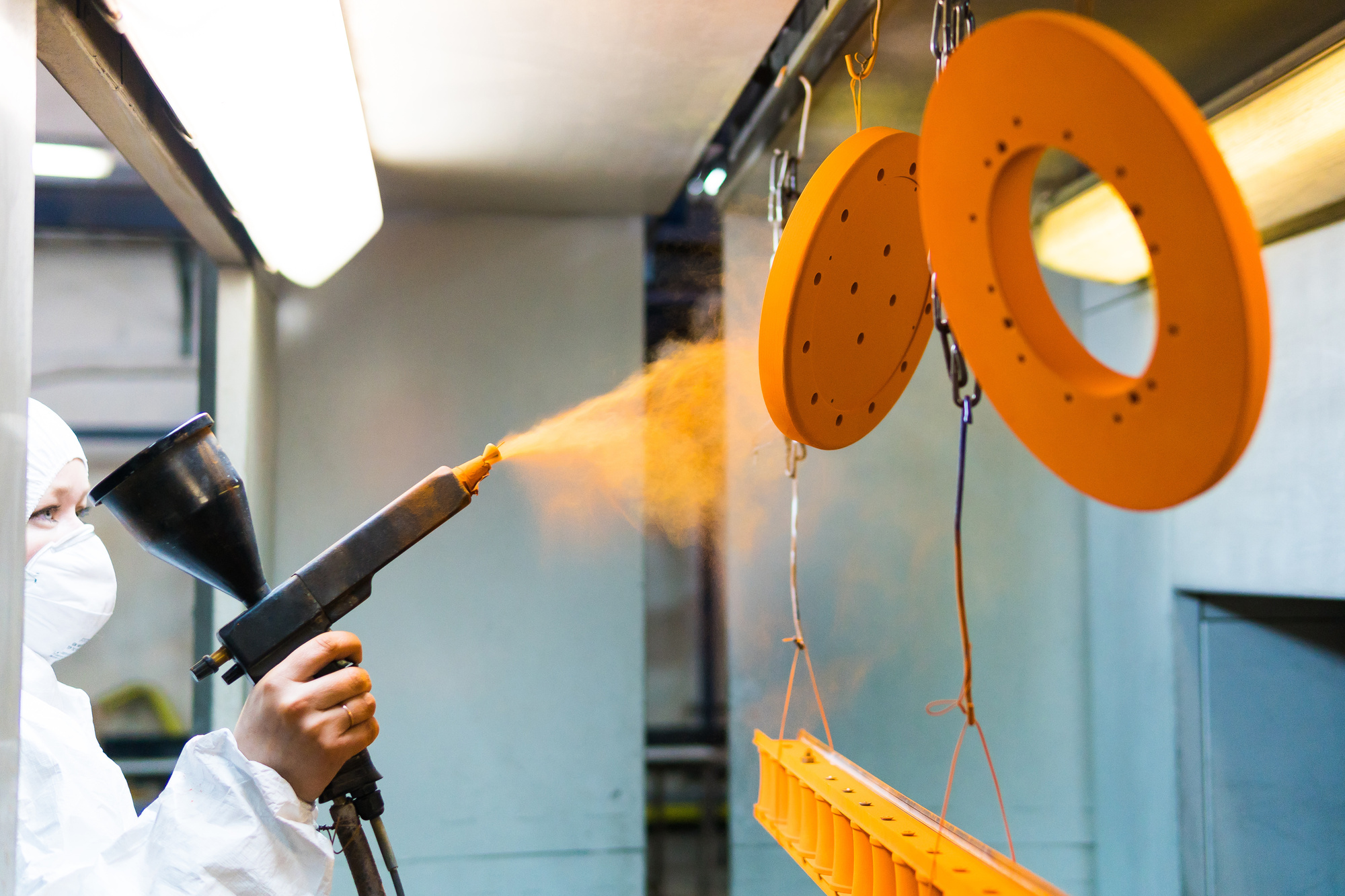 Powder coating of metal parts. A man in a protective suit sprays powder paint from a gun on metal products.